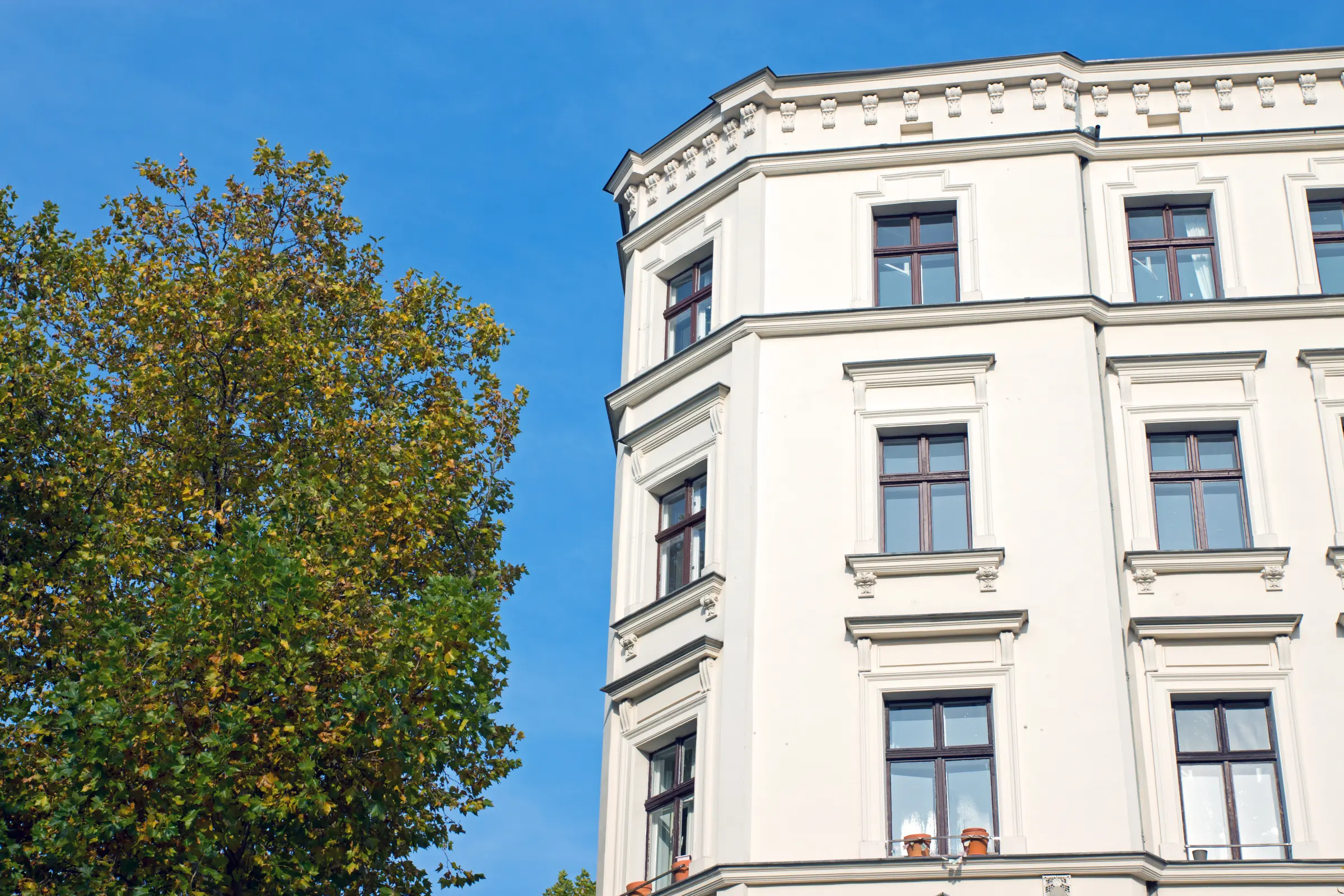 Altbau-Mehrfamilienhaus mit wenigen Wohneinheiten neben Baum – Symbol für kleine WEG